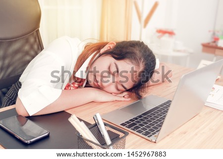 Tired Asian  business woman taking a nap on messy desk in office after work hard long time. Sleepy employee officer sleeping for relaxing.  
