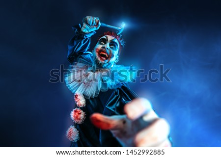 A portrait of an angry crazy clown from a horror film with a hammer. Halloween, carnival.