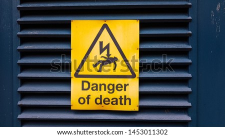 Danger of death yellow warning sign with voltage symbol and character laying down, hanging on a blue wooden door