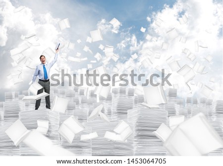 Businessman keeping hand with book up while standing among flying books with cloudly skyscape on background. Mixed media.