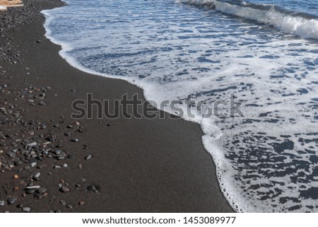 Black fine volcanic sand beach and pebbles on Bali island in Indonesia. The sea water reaches the coast and turns into sea foam. Wet black sand on the sea coast. Dark interesting background 