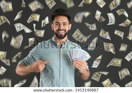 Happy young man with dollars under money rain on grey background