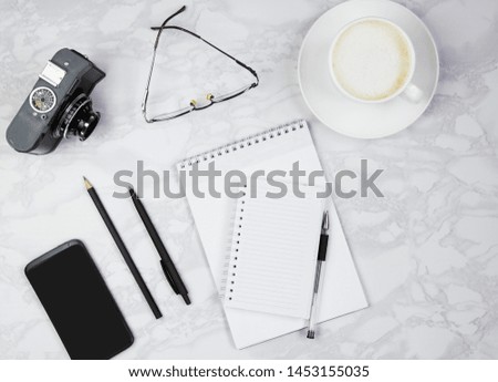Workplace with notepad, telephone, pen, glasses, camera and a cup of coffee on a marble table. Top view, flat lay, copy space