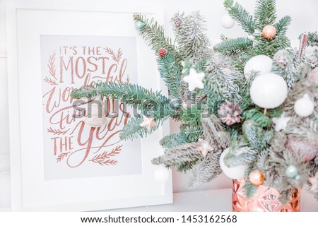 picture with Christmas inscription stands next to a vase and Christmas tree branches