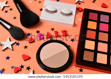 Sale text on an orange background. Professional trendy makeup products with cosmetic beauty products,  eye shadows, eye lashes, brushes and tools.