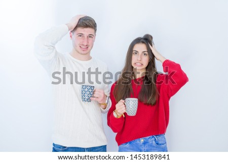 Beautiful young couple over white isolated background drinking a cup of coffee stressed with hand on head, shocked with shame and surprise face, angry and frustrated. Fear and upset for mistake.