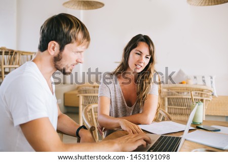 Skilled Caucasian digital nomad testing laptop application while updating system of modern netbook, serious male and female colleagues checking mail box with messages from online web clients