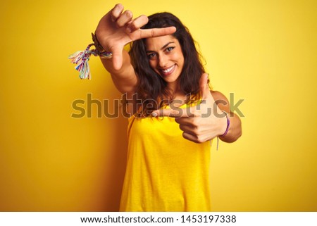 Young beautiful woman wearing t-shirt standing over isolated yellow background smiling making frame with hands and fingers with happy face. Creativity and photography concept.