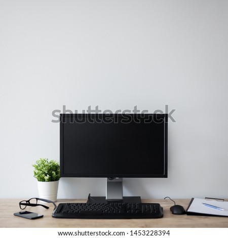 modern workplace with computer, flower pot, glasses, clipboard and pen - copy space in blank screen and over white wall