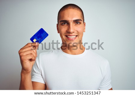 Young handsome man holding credit card over white isolated background with a happy face standing and smiling with a confident smile showing teeth