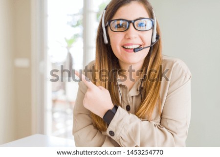 Beautiful young operator woman wearing headset at the office cheerful with a smile of face pointing with hand and finger up to the side with happy and natural expression on face