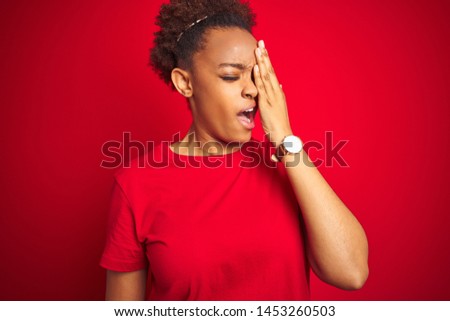 Young beautiful african american woman with afro hair over isolated red background Yawning tired covering half face, eye and mouth with hand. Face hurts in pain.