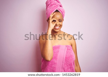 African american woman wearing shower towel after bath over pink isolated background doing ok gesture with hand smiling, eye looking through fingers with happy face.