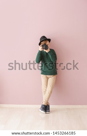 Cute little photographer with professional camera near color wall