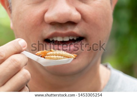 Food Insect: Man hand holding spoon eating Bamboo Worm insect or Bamboo Caterpillar deep-fried as food on white background, is good source of meal high protein edible for future. Entomophagy concept. Royalty-Free Stock Photo #1453305254