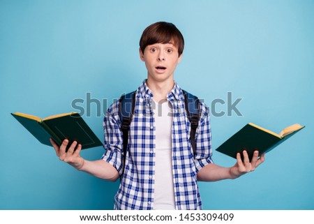 Portrait of impressed college student holding printed fiction books staring isolated over blue background