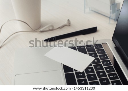 empty business card on laptop keyboard, pen and earphones on office table