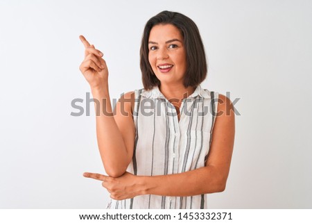 Young beautiful woman wearing casual striped shirt standing over isolated white background with a big smile on face, pointing with hand and finger to the side looking at the camera.