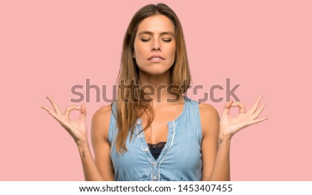 Blonde woman with jean dress in zen pose over isolated pink background