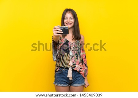 Caucasian girl in colorful dress over isolated yellow background holding a camera