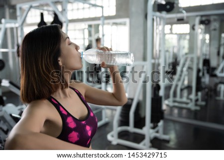 Young athletic fitness woman drinking water from bottle in gym.