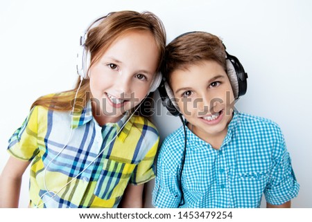 A portrait of two cheerful young kids listening to music in headphones over the white background. Summer casual kids fashion.