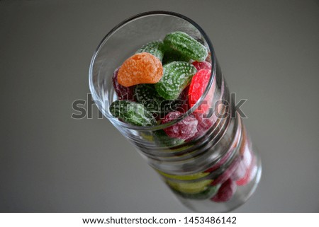 Multicolored tasty candies in a glass cup on the mirror. The reflection of the glass and sweets creates a striking effect of volume and increases the number of objects in the frame, which makes sweets