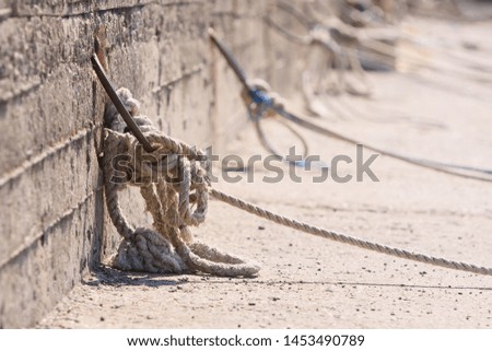Mooring ropes holding fisherman boats in port of Nessebar, Bulgaria. Close up of old nautical rope knotted on rusty metal hook in concrete wall