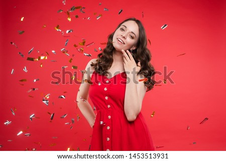 Brunette in red dress posing while sparkles falling around