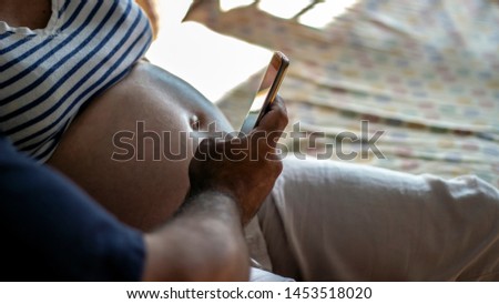 Pregnant women sitting at home while her husband taking selfie with mobile. Romantic family moment of young couple taking pictures. Happy pregnant woman and her husband taking selfie photo with mobile