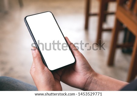 Mockup image of a woman holding black mobile phone with blank desktop screen while sitting in cafe