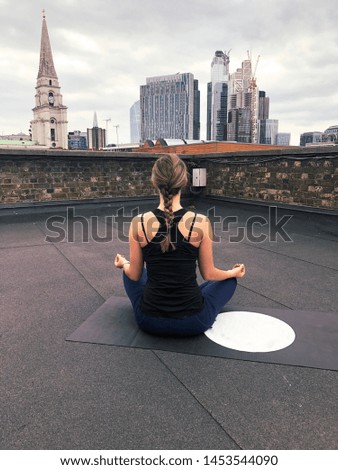 Young, athletic girl practicing yoga on rooftop in central London. View of City skyscrapers in the background. London, UK -Image