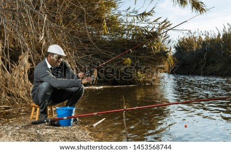 Portrait of cheerful afro fisherman sitting on wooden stool and fishing