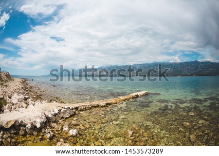 Old stone pier on the Adriatic coast. Sea coast of Croatia. Calm water. Beautiful places of European cities. Sky with clouds and mountains.