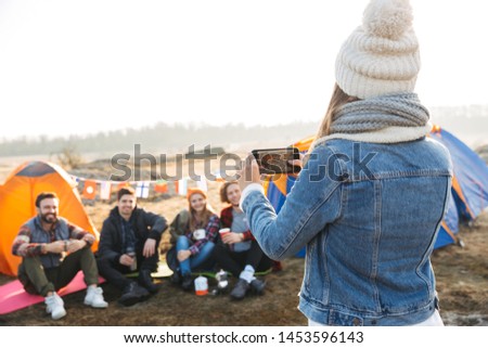 Close up of a young girl taking a picture with mobile phone of her friends sitting at the tent outdoors