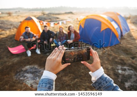 Close up of a young girl taking a picture with mobile phone of her friends sitting at the tent outdoors