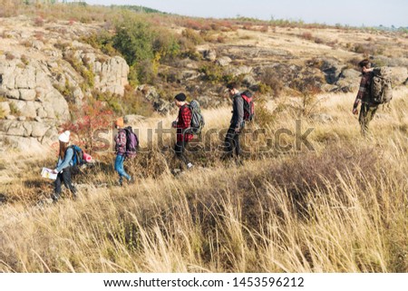 Photo of young group of friends outside in free alternative vacation camping over mountains walking with map.