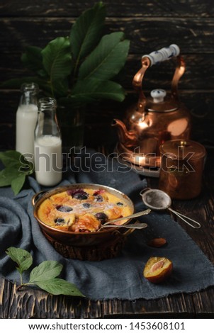 Homemade sweet plum pie clafoutis, two bottles of milk and green leaves on a dark wooden table. Close up