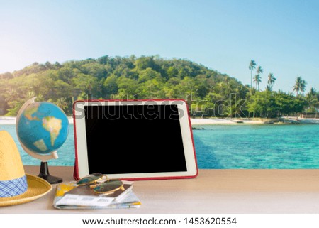 Travel accessories put on old wooden desk with a laptop, iPad, hat, sunglasses, passport and boarding pass preparations for vacation with beautiful sea background.