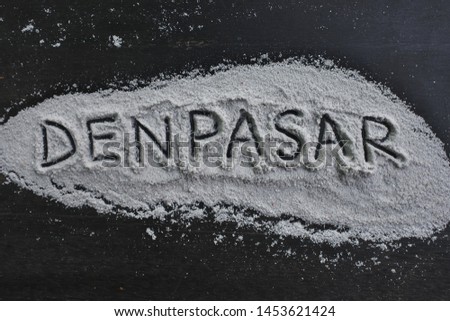 the word "Denpasar" is written in salt on a black board
