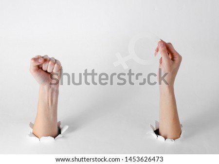 Women's hands hold the feminist gender symbol and fist through the torn holes of a white background. Creative art
