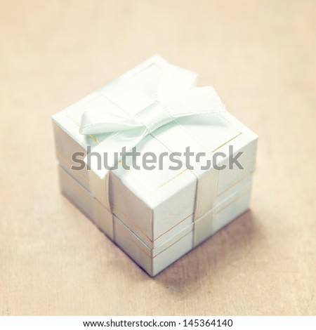 Gift box with white ribbon on beige background