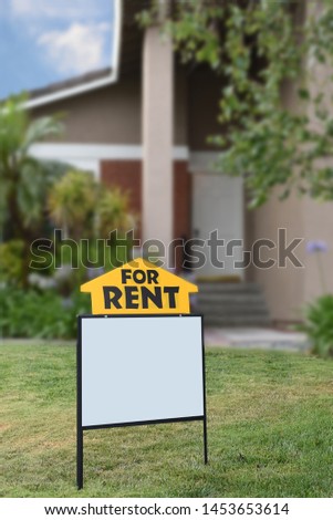 Closeup of a For Rent sign in front of a home. The house is out of focus, in vertical format.