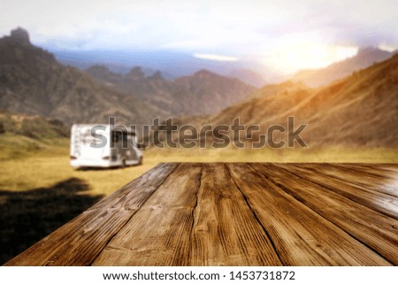 Wooden table background in the beautiful sunset in the mountains view and a camper