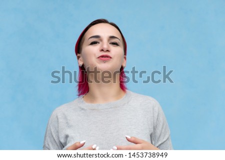 Portrait of the chest of a pretty girl with red hair on a blue background in a gray jacket. Standing in the studio right in front of the camera with emotions, talking, showing hands, smiling