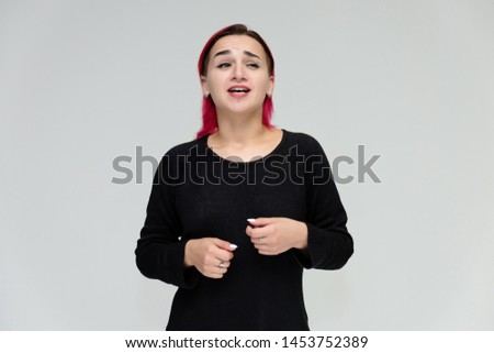 Portrait to the waist of a pretty girl with red hair on a white background in a black jacket. Standing right in front of the camera in a studio with emotions, talking, showing hands, smiling