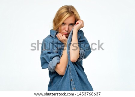 Beautiful blonde female student looks in bewilderment, being dissatisfied with something hiding with her shirt. Feeling uncomfortable concept.