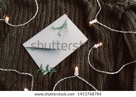 Top view on blank envelope on a warm sweater surrounded festoon lights. Cozy fall or winter flat lay. 