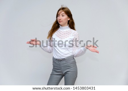 Portrait of a young beautiful brunette girl with beautiful long hair on a white background in a white jacket and gray pants. Right in front of the camera, smiling, showing emotions in various poses.