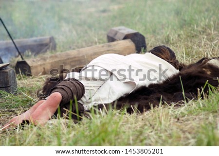 A young man in a folk shirt sleeps on a bear skin spread in the field in the summer. Camping. Festival of historical reconstruction of the Middle Ages.